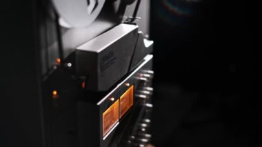 Bu video, eski bir makaradan makaraya kaset çalara odaklanıyor, kasvetli bir arkaplan karşısında dönen makaraları ile. Sıcak ışıklandırma analog ses teknolojisini vurguluyor..