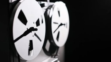 Açık bir teyp kayıt cihazının, siyah bir arka planda dönen makarasının detaylı görüntüsü. Odak hareketi yakalar, bu klasik kayıt sistemindeki bant akışını vurgular.