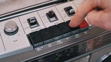 Bir parmak, eski bir teyp üzerindeki ileri sarma tuşuna basar. Klasik bir ses aygıtının yakın çekim görüntüsü, mekanik düğmeler ve eski doku vurgulanır..