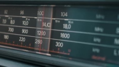 Klasik bir ses güvertesindeki radyo ayarlayıcısının detaylı bir görüntüsü. Kırmızı gösterge frekans ölçeğinde hareket eder, sayıları ve bantları vurgular.