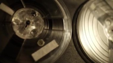 Bir banttan diğerine hareket eden dönen makaralara odaklanan, eski bir makaradan makaraya yakın çekim görüntüsü, sıcak bir ışıkla aydınlatılmış..