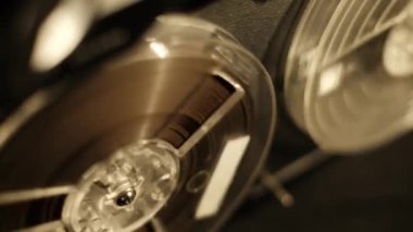 Kaset kaydedici için bir makarayı yakın çekimde sıcak ışık altında temiz hareket eden kasetlerle kapatın. Ses yakalama için daha eski bir kayıt sistemini vurgulayan net detay içeren bir vintage tasarıma odaklan.