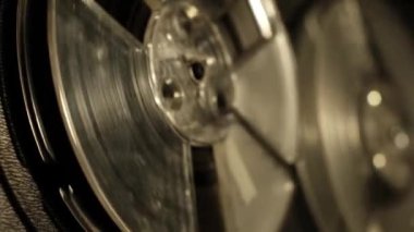 Yakın çekim, bir stüdyo ortamında geçen, analog ses kayıt sisteminin mekanik hareketini ve dokusunu vurgulayan, eski bir teybin dönen makaralarını yakalar..