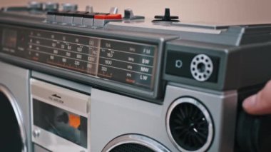 Bir el eski gümüş kasetçaların ayarlarını ayarlıyor. Radyo frekans göstergesi FM, SW, MW ve LW bantlarını göstererek ölçek boyunca hareket eder.
