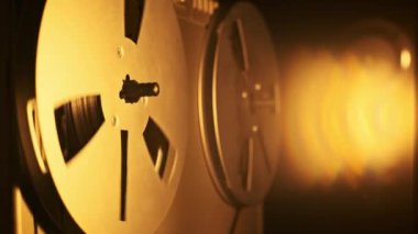 Bant döndürme ve sıcak ışık efektleri ile antika makaralı teyp teybini kapatın. Döndürme mekanizmalarına odaklanan retro cihazın altını çizerek eski moda bir kayıt ortamı oluşturun..