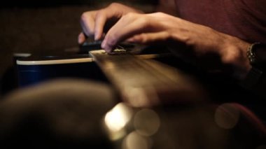 Akustik gitar çalarken gitaristin parmaklarını gitar tellerine bastıran odaklanmış, yakın plan bir fotoğraf. Bu bir gitaristin müzik yeteneği ve enstrüman kullanımı sergiliyor