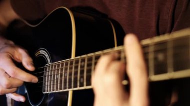 Yakın çekim videoda siyah akustik gitar çalan ve telleri seçen bir adam görülüyor. Bu video gitar panosundaki ayrıntıları vurgular ve harika bir müzikal görsel sunar..