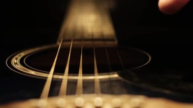 Parmak karıştırma, akustik gitarda düşük karanlık ışıkta ayrı teller. Tellerin ayrıntıları ve karanlık, gölgeli aydınlatma ve sığ alan derinliğine karşı açılan delik samimi bir görüntü oluşturur.