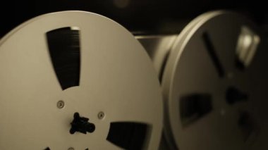 Eski bir makaradan makaraya kayıt cihazının yakın çekim görüntüsü dönüyor. Hareket, hareketin ve retro estetiğin vurgulandığı karanlık bir arkaplana karşı analog kayıt sürecini vurguluyor.
