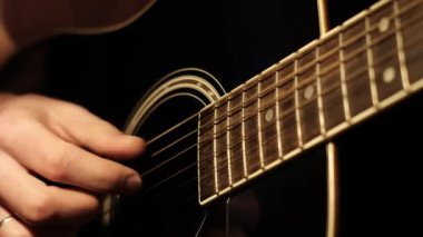 Düşük ışık koşulları altında akustik gitarın tellerini koparan eller, tıngırdayan parmakları vurgular. Geceleri evde enstrüman çalmak için detaylı bir bakış açısı..