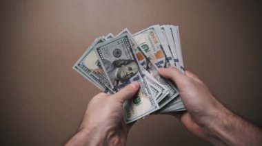 Bir kişi 100 dolarlık banknotları sayıp sergiliyor. Finansman veya ekonomik içerik için ideal.