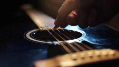 Yakın plan çekimde gitar tellerine vuran bir gitar penası, yumuşak bir stüdyo ışığı altında gösteriliyor. Görünüm gitar gövdesini ve köprüyü keskin bir odak noktasında içerir ve dizgiler eylem yaratır.