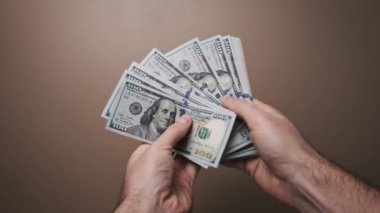 Bir kişi tarafsız kahverengi stüdyo geçmişi, refah, gelir ve başarı fikirleri olan ABD para destesini iki eliyle manipüle ediyor..