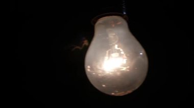 Gözle görülür bir ipliğe sahip parlak bir ampul sarkıyor, simsiyah bir arka plana sıcak bir parıltı saçıyor.