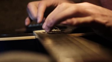 Akustik gitar boynu boyunca akorlar için konum alan eller ve parmaklar aşırı yakın plan. Parmak pozisyonları ve sicim etkileşimi hakkında özel detay, yumuşak ışık altında yakalanır.
