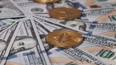 Altın bir Bitcoin sikke, geleneksel ve kripto para birimlerini birlikte gösteren 100 dolarlık banknotlardan oluşan bir yataktaki birden fazla madeni paradan biridir..