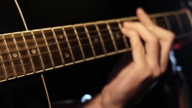 Yakından bakıldığında, siyah bir akustik gitar çalarken akorları oluşturan, akor ilerlemelerini ve müzikal becerileri gösteren parmaklar fretboard 'a bastırılmış..