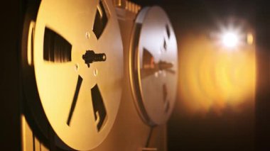 Dönen makaralı, eski bir makaradan makaraya yakın çekim. Lens ışığı, geçmişe dönük estetiği ve analog kayıt sürecini vurgulayarak, karanlık bir arkaplan karşısında sahneyi vurgular.