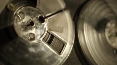Mekanik bileşenleri, hareketi ve sıcak stüdyo ışığını vurgulayan retro-reel-to-reel oynatıcıda dönen iki bant makarasının yakın görüntüsü klasik, klasik bir ortam yaratıyor..
