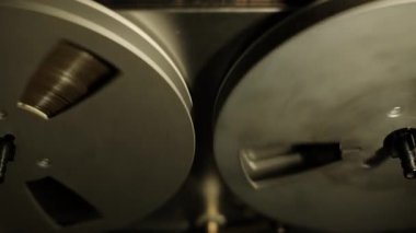 Dönüşlerine ve hareketlerine odaklanan iki klasik makaralı teyp makarası iş başında. Bir retro analog kayıt süreci mekanik elementlere vurgu yapan karanlık bir arkaplan karşısında yakalanır.