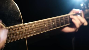 Parlak bir spot ışığı altında, eller akustik bir gitarın boynundaki akort formlarını ve hareketleri oluşturur çünkü sanatçı ayrıntılı parmak tekniklerini sergiler..