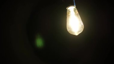 Klasik bir Edison ampulü askıya alınır, ipliği parlak bir şekilde siyah bir arkaplanda parlar, ampul tasarımının karmaşık detaylarını vurgular.