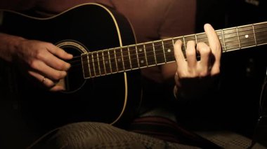Gitar akorları yapan bir adamın ellerine odaklanan video. Video, siyah akustik gitar çalarken ellerinin fretboard 'da olduğunu vurguluyor..