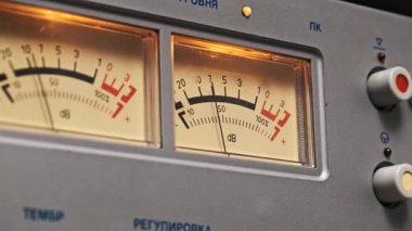 Kaliteli turuncu ışıltılı VU sayacına yakın çekim. Göstergeler desibel seviyelerini gösteriyor, klasik ses donanımını çağrıştırıyor. Müzik üretimi, retro teknoloji ve ses mühendisliği temaları için ideal