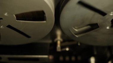 Yukardan aşağı yakın çekim, senkronize dönen makaralı makaralar. Eski bir ses sisteminin koyu metalik dokusunu ve hareketini vurgulayarak mekanik analog kayıt detaylarını gösterir.