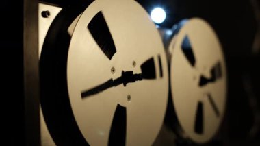 Eski bir makaradan makaraya kayıt cihazını kapat, makaralar dönerek, karanlık bir arkaplana karşı dinamik detaylarla görüntülenir, geriye dönük hareketi vurgular, ve kaset