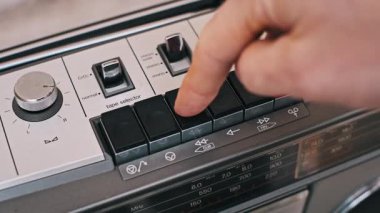 Klasik bir kaset destesindeki geri sarma tuşuna elle basıyor. Eski okul oyuncusunun mekanik yönlerine ve düğme kontrollerine odaklanan bir yakın plan.