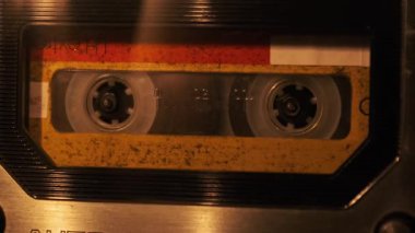 The cassette is played in a tape recorder in soft flickering candlelight, close-up. Yellow audio cassette in the deck rotates. Vintage sound recording in an old retro recorder. Audio Cassette playback