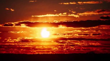 Ateşli turuncu bir günbatımının zamanı. Güneş dramatik bulutların arasında parlıyor. Karanlık bir ufuk üzerinde canlı ve dinamik bir gökyüzü yaratıyor..