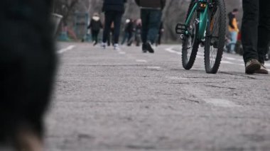 Düşük açılı bir bisiklet görüntüsü ve şehir parkında yürüyen insanlar. Arka planda bulanık bir köpek var..