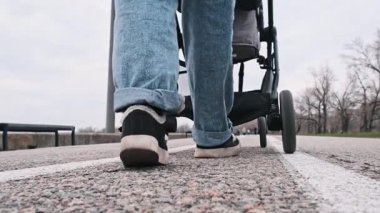 Kotlar ve spor ayakkabılar giyen bir insan, bulutlu bir günde asfalt bir yolda bebek arabasını itiyor. Düşük bir perspektiften çekiliyor..