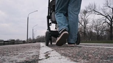 Kotlu bir kişinin, arka planda lamba direkleri ve ağaçlarla birlikte asfalt bir yolda bebek arabasını iterken düşük açılı görüntüsü..