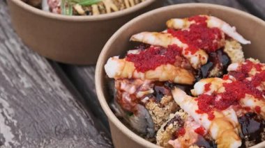 Yakın çekim yavaş tavada karides, kırmızı tobiko havyarı ve paket kâğıt kasede koyu soslu lezzetli suşi ruloları görülüyor. Kırsal ahşap arka planda Japon sokak yemekleri kavramı.