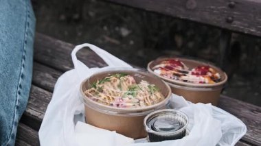 Suşi sosisi ya da karton kutularda paketlenmiş suşi hamburgerleri ahşap bir bankta teslimat torbasında duruyor. Fusion sokak yemekleri, uygun bir açık hava yemeği ya da şehir pikniği için mükemmel..
