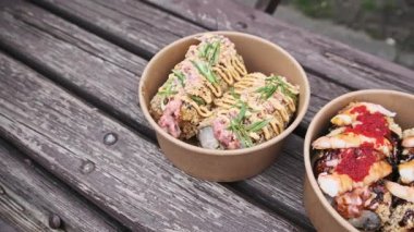 İki farklı suşi köpeğinin yakın çekim görüntüsü, modern bir füzyon tabağı, çevre dostu kağıt kaselerde servis ediliyor. Lezzetli Japon sokak yemekleri ahşap bir bankta servis edilir..