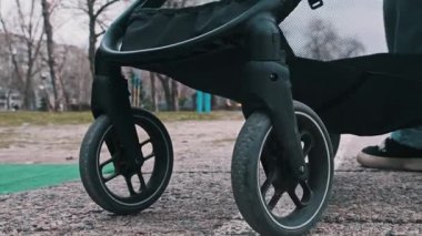 Parkın çimenli bir köşesine park edilmiş kaldırımlı yolda duran bebek arabasının düşük açılı görüntüsü, bir aile yürüyüşü sırasında duraksamayı akla getiriyor..