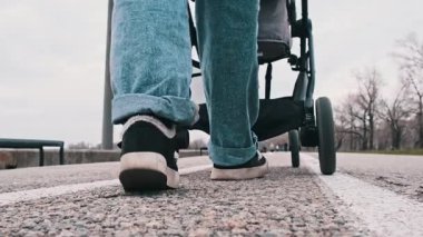 Bir kadın, çim ve ağaçlarla çevrili bir yolda bebek arabasını itiyor. Parkta sakin bir yürüyüşün zemin katındaki manzarası..