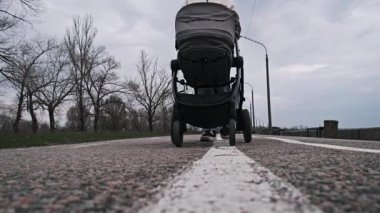 Alçak açılı, yakın plan bebek arabalarının tekerlekleri ve şehir yolunda yürüyen insanların ayakları..