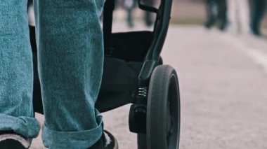 Bebek arabasını kaldırımlı bir yolda iten birinin düşük açılı görüntüsü, ayaklar ve bebek arabasının tekerlekleri görünür..