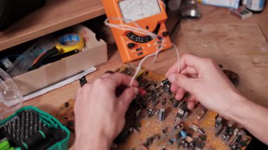Analog çokölçer kullanan bir elektronik teknisyenin yakından görüntüsü bileşenleri test etmek ve kompleks baskılı devre kartındaki gerilimi veya direnci ölçmek için tanılama sırasında veya onarım çalışmaları sırasında