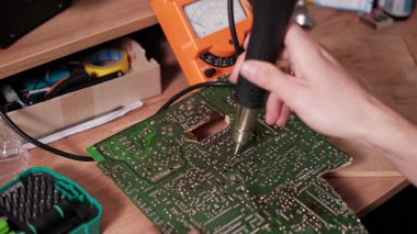 Bir elektronik teknisyeninin yeşil baskılı devre kartının PCB 'sini tamir atölyesinde ısıtmak ve lehimlemek için sıcak hava istasyonu aracını kullanırken yakın plan görüntüsü.