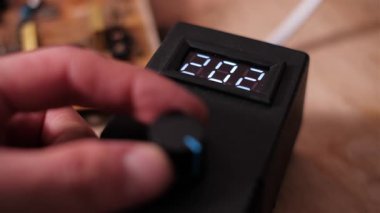 Parlak bir LED ekranda gösterilen sayısal voltaj değerini azaltarak, parmaklar bir kontrol düğmesini döndürür. Teknoloji atölyesindeki özel bir cihazın elektrik parametre ayarlarını kapat.