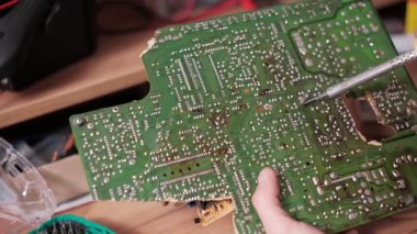 Teknisyen karmaşık yeşil baskılı devre kartında lehimleme yapıyor. Tahtayı sabit tutarken aynı zamanda bir elektronik atölyesindeki lehim eklemlerine sıcak demir ucunu uyguluyor..