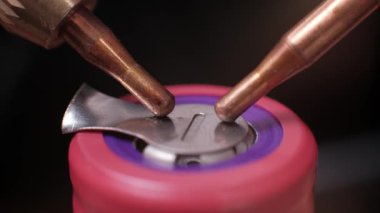 Aşırı yakın plan, bakır kaynaklama sondalarının 18650 model pembe bir lityum iyon bataryasına nikel şerit taktığını gösteriyor. Özel pil imalatı ve enerji çözümlerinde kullanılan yüksek hassasiyetli bir işlem.