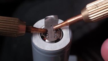 Nikel şeridi ile gri bir lityum-iyon 18650 pil hücresinin pozitif terminaline bağlayan nokta kaynaklama sürecinin yakın görüntüsü koyu arkaplan üzerinde bakır elektrotlar kullanılarak.