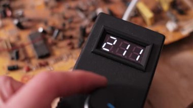 Elektronik cihazın düğmesini çeviren el, dijital görüntü okumalarının hızla azalmasına neden oluyor. Yakın plan bir atölyede elektriksel değer numaralarını göstererek voltaj değişimini gösterir.